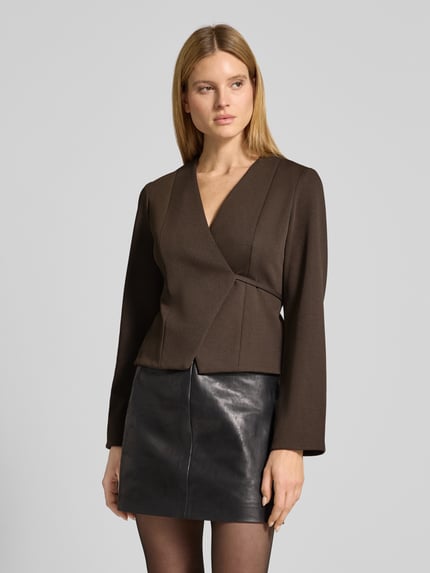 Modelka nosi żakiet z elastycznej mieszanki materiałów, krój taliowany, model 'Simmi' od Neo Noir, dekolt w serek, taśma do wiązania, kopertowy styl, długość tyłu w rozmiarze 36: 52 cm, szerokość w rozmiarze 36: 40 cm, długość rękawów w rozmiarze 36: 63 cm, kolor ciemnobrązowy, gładka tekstura, widok całej sylwetki z przodu.