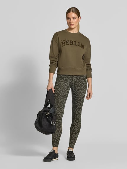 Frauenmodel trägt Sweatshirt mit Label-Print von Lala Berlin in Khaki mit Rundhalsausschnitt und gerippten Abschlüssen, Baumwolle, Ganzkörperansicht von vorne.