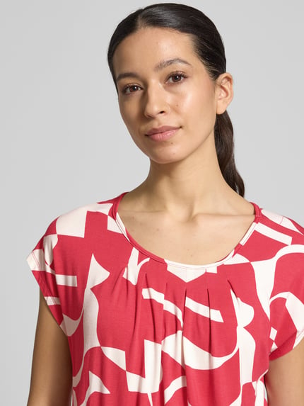 Kobiece modelka nosi bluzkę Regular Fit Bluse aus Viskose-Mix Modell 'Minou' od ZABAIONE, czerwony nadruk na całej powierzchni, mieszanka wiskozy, okrągły dekolt, krótki rękaw, elastyczny pas, długość tyłu w rozmiarze S: 62 cm, zbliżenie na górną część ciała.