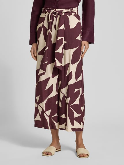 Frauenmodel trägt Stoffhose aus Viskose-Mix mit Bindegürtel Modell 'PLUMAS' von Mango, Allover-Look in Creme und Bordeaux, Nahaufnahme Unterkörper.