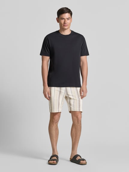 Männermodel trägt Regular Fit Shorts aus reiner Baumwolle Modell 'REGCAL' von SELECTED HOMME, beige mit Streifen, Ganzkörperansicht von vorne.