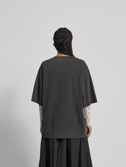 Männermodel trägt Oversized T-Shirt mit Label-Stitching von black palms z bawełny, krój oversized, okrągły dekolt, przetarcia, długość tyłu 77 cm, całkowity widok od tyłu.