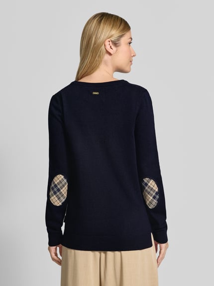 Frauenmodel trägt Regular Fit Pullover aus Woll-Baumwoll-Mix von Barbour in Dunkelblau mit karierten Ellbogenpatches, Ganzkörperansicht Rückansicht. Damen Rollkragenpullover von Barbour.