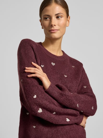 Frauenmodel trägt Strickpullover mit Stitchings und Rundhalsausschnitt von Apricot, burgunderfarbener Material-Mix, Nahaufnahme Oberkörper.
