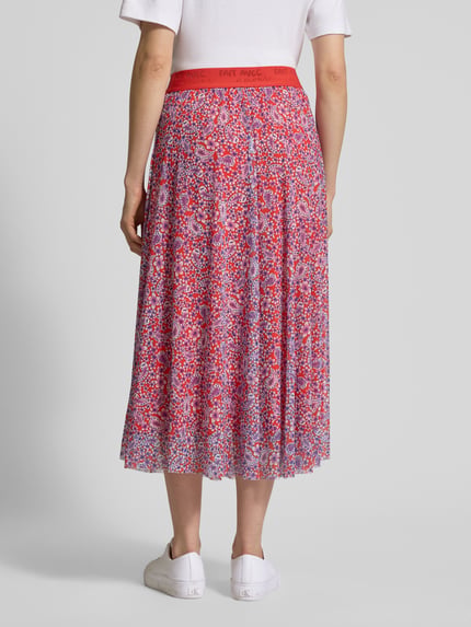 Frauenmodel trägt Midirock mit elastischem Bund von Smith and Soul in Rot mit buntem Blumenmuster und blickdichtem Unterrock, Ganzkörperansicht Rückansicht.