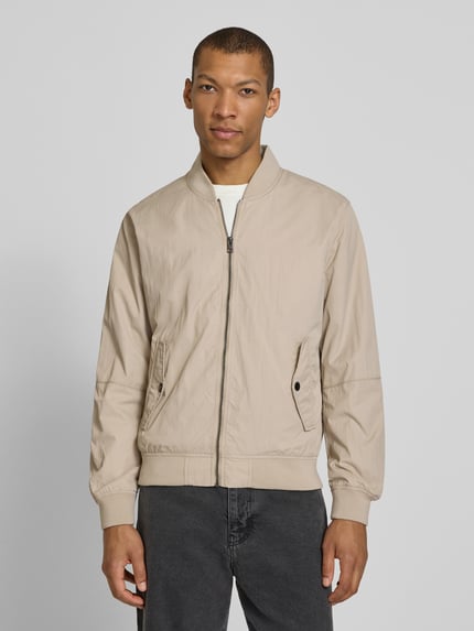 Männermodel trägt Regular Fit Bomberjacke mit Stehkragen von s.Oliver RED LABEL in Beige, unifarben, Reißverschluss, Ganzkörperansicht von vorne.
