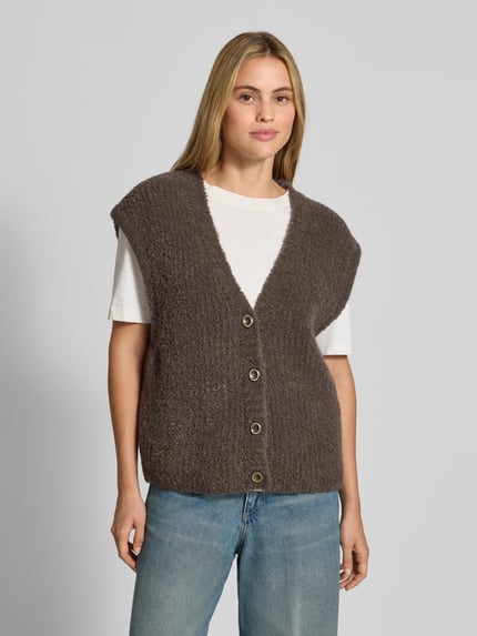 Kobiece model nosi kamizelkę Relaxed Fit Weste mit Alpaka-Anteil Model 'Zolly' od American Vintage, mieszanka bawełny i wełny z alpaki, imitacja dzianiny, listwa guzikowa, dekolt w serek, długość tyłu w rozmiarze XS/S: 57 cm, widok całej sylwetki z przodu.
