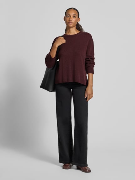 Frauenmodel trägt bordeauxroten Loose Fit Pullover aus reiner Wolle von Marc O'Polo, kombiniert mit schwarzer Hose, Ganzkörperansicht von vorne. Damen Pullover von Marc O'Polo.