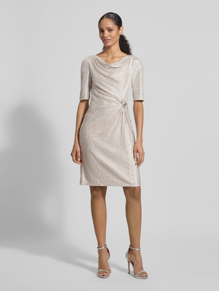 Frauenmodel trägt knielanges Cocktailkleid mit Wasserfall-Ausschnitt von Vera Mont in Beige, taillierte Passform mit Raffungen, Ganzkörperansicht von vorne.