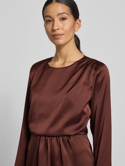 Frauenmodel trägt Knielanges Cocktailkleid mit Rundhalsausschnitt von Rinascimento aus braunem Satin, körpernahe Passform, Nahaufnahme Oberkörper.