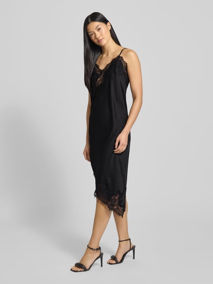 Frauenmodel trägt Kleid aus Satin mit Spitze Modell 'Sorelle' von Neo Noir, schwarzer Satin, Asymmetrischer-Look, Minikleid mit Spaghettiträgern, Ganzkörperansicht von vorne.