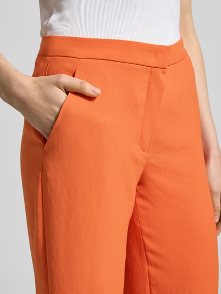 Frauenmodel trägt orange Hose mit Eingrifftaschen, Modell 'PALINA 6/8' von Raffaello Rossi, verkürzte Passform, Nahaufnahme Oberschenkel.