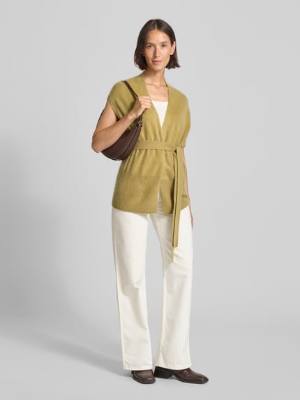 Vrouwenmodel draagt Loose Fit Strickweste aus Kaschmir-Woll-Mix van HERZENS in lichtgroen, open voorkant, mouwloos, bindriem, zachte textuur, ruglengte 68 cm bij maat 36, volledig lichaam vooraanzicht.