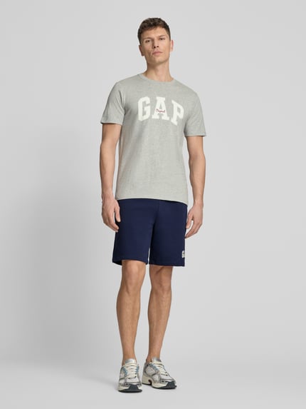 Männermodel trägt Sweatshorts mit elastischem Bund von GAP, Baumwoll-Mix, Relaxed-Fit, Logo, dunkelblau, Ganzkörperansicht von vorne.