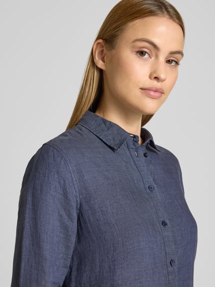 Modelka kobieca ma na sobie Leinenbluse mit Label-Detail und Hemdblusenkragen od Fynch-Hatton, czysty len, krój regular fit, niebieski kolor, faktura lnu, zapięcie na guziki, długość tyłu w rozmiarze 36: 63 cm, długość rękawa: 62 cm, półzbliżenie na górną część ciała.