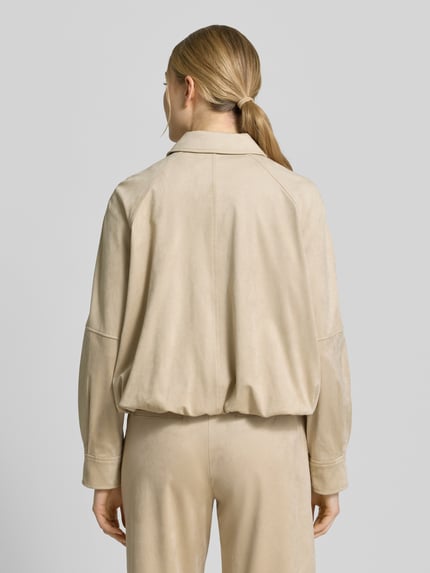 Vrouwenmodel draagt Jacke mit Knopfleiste und Eingrifftaschen Modell 'Nayomi' van Someday in beige, relaxed fit, mix van materialen met stretch, opstaande kraag, zichtbare knopen, steekzakken, achterlengte 52 cm, schouderbreedte 42 cm, borstwijdte 66 cm, mouwlengte 60 cm. Volledige lichaamsopname achteraan.