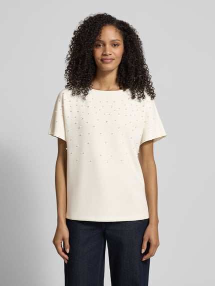 Modelka kobieca ma na sobie T-shirt mit Rundhalsausschnitt und Perlen von Christian Berg Woman z mieszanki materiałów z modalu, krój relaxed fit, okrągły dekolt, perły, widok całej sylwetki od przodu.