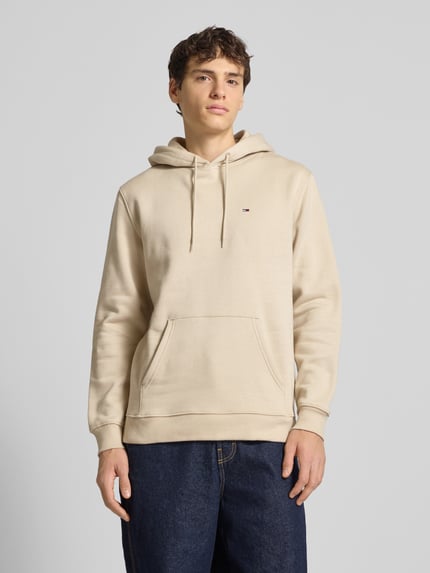 Männermodel trägt Regular Fit Hoodie aus Baumwoll-Mix von Tommy Jeans, unifarben, langarm, logo, fleece textuur, Ganzkörperansicht von vorne.