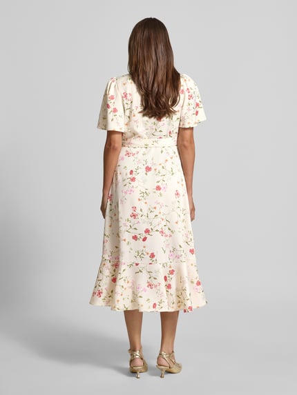 Frauenmodel trägt Cocktailkleid in Wickel-Optik Modell 'THEA' von YAS mit floralem Allover-Look, Material-Mix, A-Linie, Midikleid, Ganzkörperansicht Rückansicht.