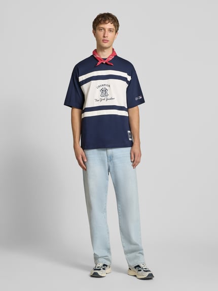 Männermodel trägt Relaxed Fit T-Shirt aus reiner Baumwolle von Champion, blau-weiß mit Logo-Print, Rundhalsausschnitt, Ganzkörperansicht von vorne.