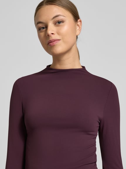 Kobiece modelka ma na sobie Slim Fit Longsleeve mit Stehkragen od Fabletics z elastycznej mieszanki materiałów, krój slim fit, stójka, z długim rękawem, długość tyłu w rozmiarze S 50 cm, kolor ciemnośliwkowy, gładka tekstura, zbliżenie na górną część ciała, widok z przodu