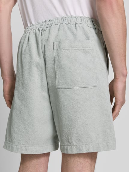Männermodel trägt Regular Fit Shorts aus Baumwoll-Mix Modell 'SANDREW' von BOSS Orange, efekt: jednolity kolor, jednolita faktura twill-jacquard, naszywka z logo, szlufki na pasek, zapięcie na guzik i kryty zamek błyskawiczny, kieszeń z tyłu, boczne wpuszczane kieszenie, wykończenie: mieszanka bawełny; Ganzkörperansicht Rückansicht.