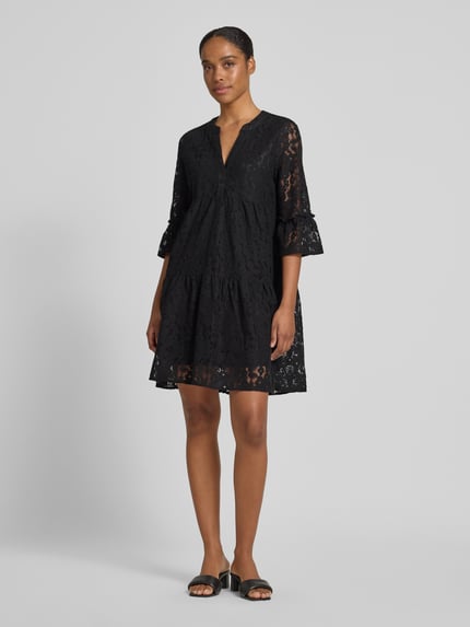 Frauenmodel trägt Loose Fit Spitzenkleid aus Baumwoll-Mix Modell 'HONEY' von Vero Moda, Optik: Unifarben, Spitzen-Muster, V-Ausschnitt, 3/4-Arm, Glockenärmel, knielang, Materialverarbeitung: Spitze, Farbe Schwarz, Ganzkörperansicht von vorne.
