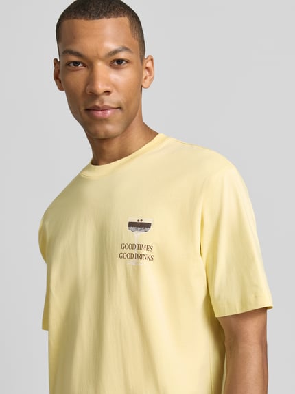 Männermodel trägt T-Shirt mit rückseitigem Motiv-Print von MCNEAL in Gelb, gerade Form, Bio-Baumwolle, Nahaufnahme Oberkörper.