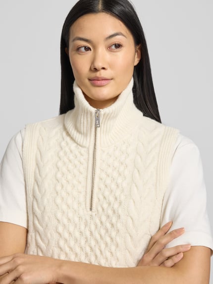 Frauenmodel trägt Relaxed Fit Pullunder aus reinem Woll-Mix Modell 'OLAIAAS CABLE' von Armedangels, Optik: Unifarben/Strukturiert, Label-Patch, Troyer-Kragen, Strick, Nahaufnahme Oberkörper.