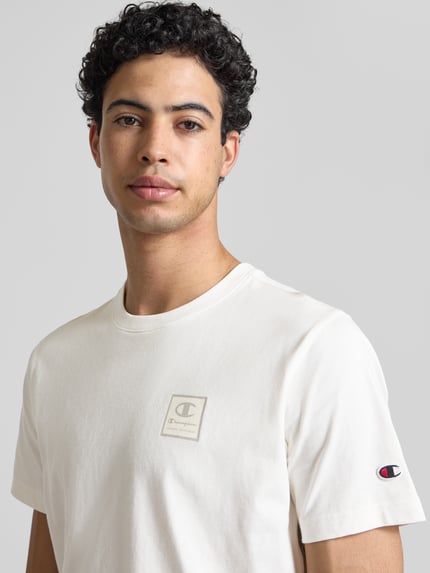 Männermodel trägt T-Shirt mit Logo und Rundhalsausschnitt von CHAMPION aus Reine Baumwolle, Regular-Fit, Rückenlänge bei Größe M 68 cm, Nahaufnahme Oberkörper.