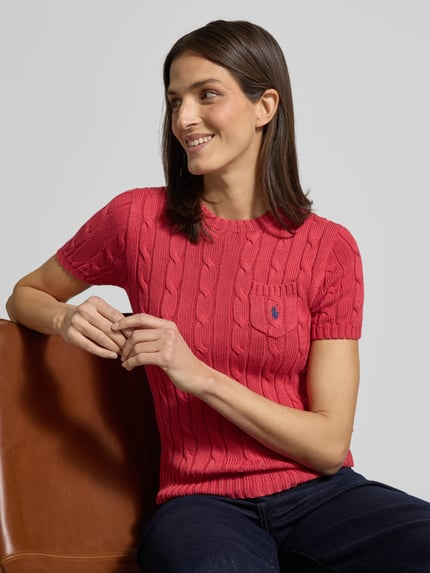 Frauenmodel trägt Slim Fit T-Shirt in Strick-Optik von Polo Ralph Lauren in Rot mit Rundhalsausschnitt, Brusttasche, Logo-Stitching, reine Baumwolle, elastische Abschlüsse, Nahaufnahme Oberkörper.