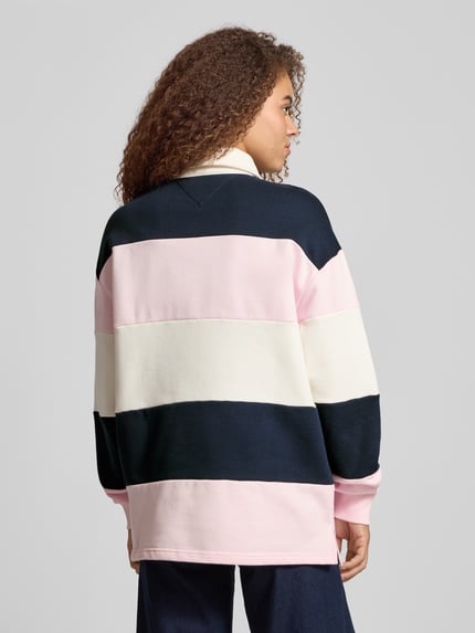 Frauenmodel trägt Regular Fit Pullover aus reiner Baumwolle von Tommy Jeans in mehrfarbiger Optik mit Label-Stitching-Applikation, Sweat-Material, gerippten Abschlüssen, Polokragen und Langarm, Ganzkörperansicht Rückansicht.