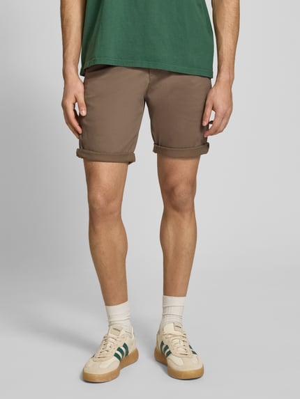 Męski model nosi Regular Fit Shorts mit Eingrifftaschen Modell 'BOWIE' od Jack & Jones, bawełna z elastanem, brązowy, krój regular fit, szerokość w rozmiarze M: 43 cm, długość wewnętrzna nogawki w rozmiarze M: 26 cm, widok całej sylwetki z przodu.
