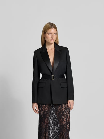 Modelka nosi Blazer mit Schurwoll-Anteil od Victoria Beckham, czarny, z domieszką wełny, krój taliowany, kołnierz z klapami, pasek w talii, kieszeń na piersi, długość pleców w rozmiarze 36: 78 cm, szerokość w rozmiarze 36: 50 cm, długość rękawa w rozmiarze 36: 66 cm, całkowity widok z przodu.