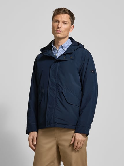 Männermodel trägt Regular Fit Funktionsjacke mit Kapuze von Tommy Hilfiger, Optik: Unifarben, wasserabweisend, Ganzkörperansicht von vorne.