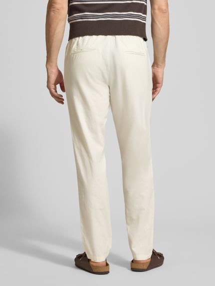 Męski model nosi Straight Fit Leinenhose mit elastischem Bund Modell 'Barton' von Matinique, mieszanka lnu i bawełny, kolor jasny, spodnie z prostymi nogawkami, elastyczny pas z tunelem, kieszenie z tyłu, szerokość w rozmiarze M: 34 cm, długość wewnętrzna nogawki w rozmiarze M: 78 cm, widok całej sylwetki z tyłu.