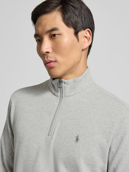 Männermodel trägt Sweatshirt mit Label-Stitching von Polo Ralph Lauren, hellgrau, Baumwoll-Viskose-Mix, Nahaufnahme Oberkörper. Lockerer-Schnitt, Stehkragen, kurzer Reißverschluss, Gerippte-Abschlüsse.