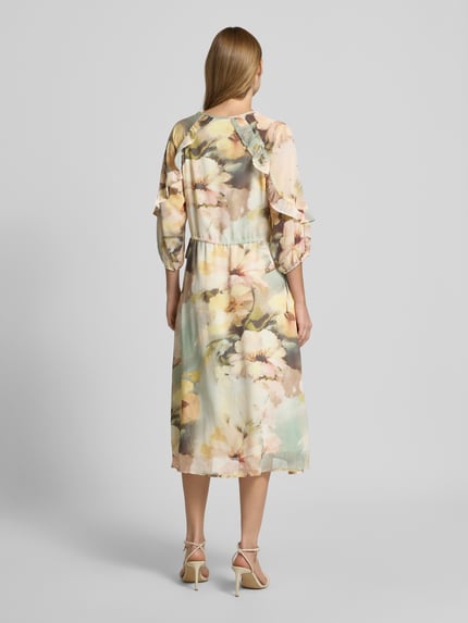 Frauenmodel trägt Midikleid mit V-Ausschnitt von Soyaconcept, florale Farben, Leicht taillierte Passform, 3/4-Arm, Rüschenbesatz, Midilänge, Rückenlänge Größe S 128 cm, Brustweite 40 cm, Ärmellänge 42 cm, Ganzkörperansicht Rückansicht.