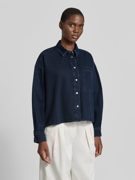 Frauenmodel trägt Relaxed Fit Jeansbluse aus reiner Baumwolle Modell 'NALAANI' von ARMEDANGELS in Dunkelblau mit silbernen Knöpfen, Ganzkörperansicht von vorne, Damen Jeansbluse von ARMEDANGELS.