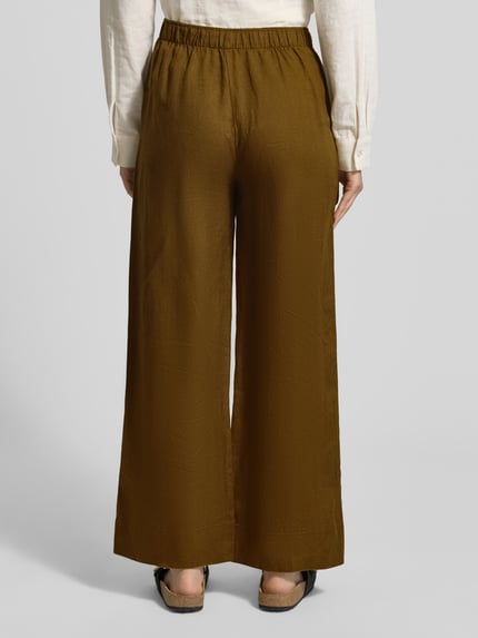 Frauenmodel trägt Leinenhose mit elastischem Bund Modell 'LINO' von Mango in Braun, Reines Leinen, Relaxed-Fit, Ganzkörperansicht Rückansicht.