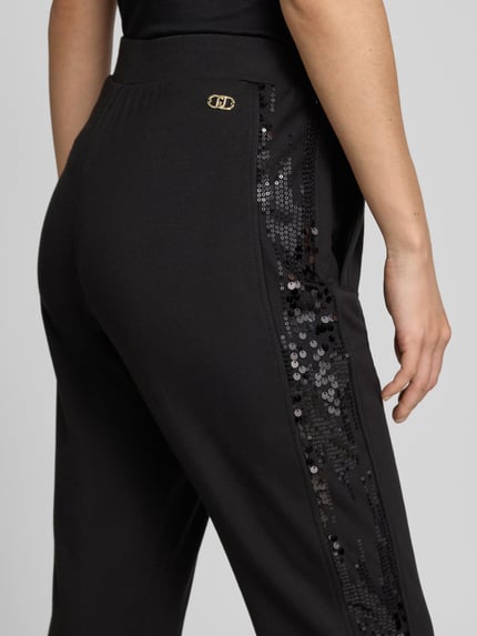 Frauenmodel trägt Sweatpants aus Viskose-Elasthan-Mix mit Pailletten von Liu Jo, schwarzer Stoff, glänzende Pailletten, Nahaufnahme Hüfte.