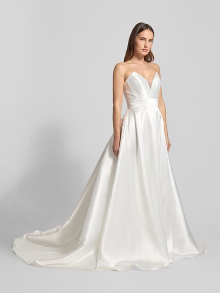 Frauenmodel trägt Regular Fit Brautkleid mit Zierknopfleiste von Luxuar in weißem Satin, taillierte Passform, ärmelloses Design, Ganzkörperansicht von vorne.