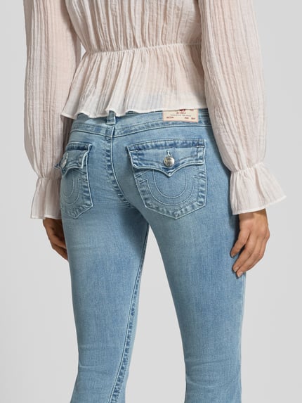 Vrouwenmodel draagt Low Rise Flared Jeans met steekzakken model 'JOEY' van TRUE RELIGION, denim in used-look, detailopname achteraan.