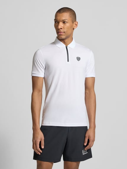 Männermodel trägt Slim Fit Poloshirt aus Viskose-Mix von EA7 Emporio Armani in Weiß mit Logo-Detail, elastischen Abschlüssen, Ganzkörperansicht von vorne.