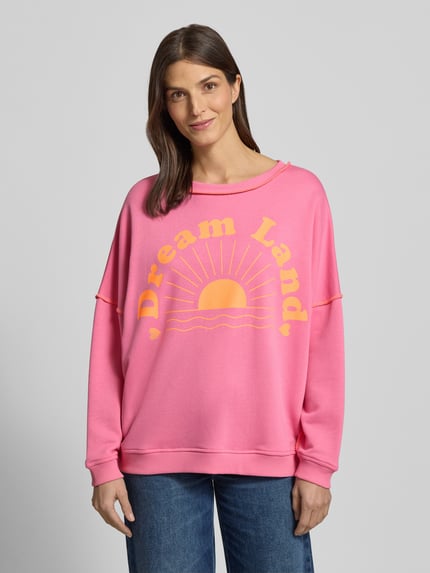 Frauenmodel trägt Oversized Sweatshirt mit gerippten Abschlüssen von miss goodlife in Pink mit gelbem Statement-Print, Nahaufnahme Oberkörper.