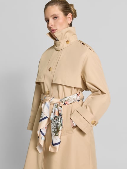 Vrouwenmodel draagt Trenchcoat met Bindegordel van Liu Jo White, katoenmix, regular fit, platte kraag, knoopsluiting, strikceintuur, ruglengte 112 cm, schouderbreedte 48 cm, borstwijdte 56 cm, mouwlengte 58 cm, zandkleur, gladde textuur, vooraanzicht van bovenlichaam.