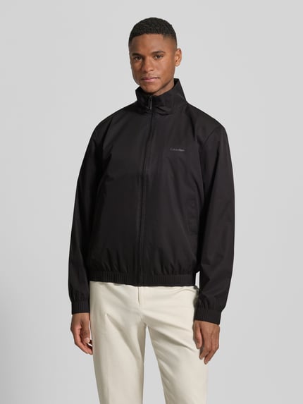Männermodel trägt Jacke mit Stehkragen und Logo von CK Calvin Klein in Schwarz, Regular Fit, Reißverschluss, Eingrifftaschen, Nahaufnahme Oberkörper