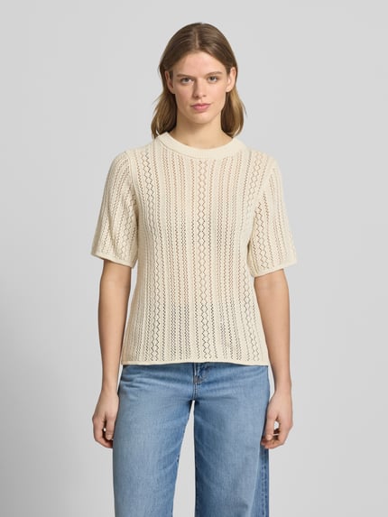 Frauenmodel trägt Regular Fit Strickshirt aus reiner Baumwolle Modell 'NUKA' von Pieces mit Optik:Allover-Muster, gestreift, Lochstrick, Rundhals, Kurzarm, cremefarbene Struktur, Ganzkörperansicht von vorne.
