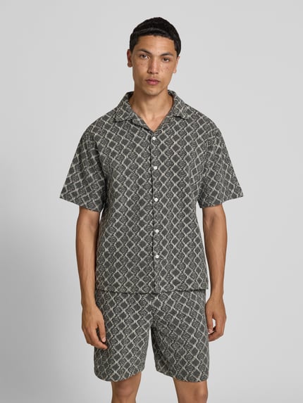 Männermodel trägt Boxy Fit Freizeithemd im Allover-Look Modell 'ZANDER' von Redefined Rebel aus Reine Baumwolle, Ganzkörperansicht von vorne. Rückenlänge bei Größe M: 65 cm, Schulterbreite bei Größe M: 51 cm, Ärmellänge bei Größe M: 25 cm, Reverskragen, graue Muster, strukturierte Oberfläche.