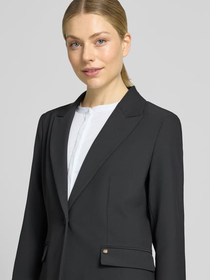 Frauenmodel trägt Regular Fit Blazer mit Reverskragen Modell 'Leonora' von MOS MOSH, glatte schwarze Oberfläche, Nahaufnahme Oberkörper. Rückenlänge 66 cm, Brustweite 40 cm, Ärmellänge 62 cm, Knopfverschluss.